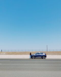 A solitary blue car parked by the roadside in Al Batinah North, Oman under a clear blue sky.
