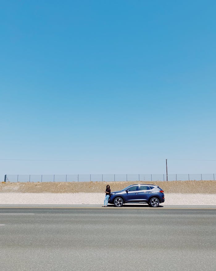 A solitary blue car parked by the roadside in Al Batinah North, Oman under a clear blue sky.